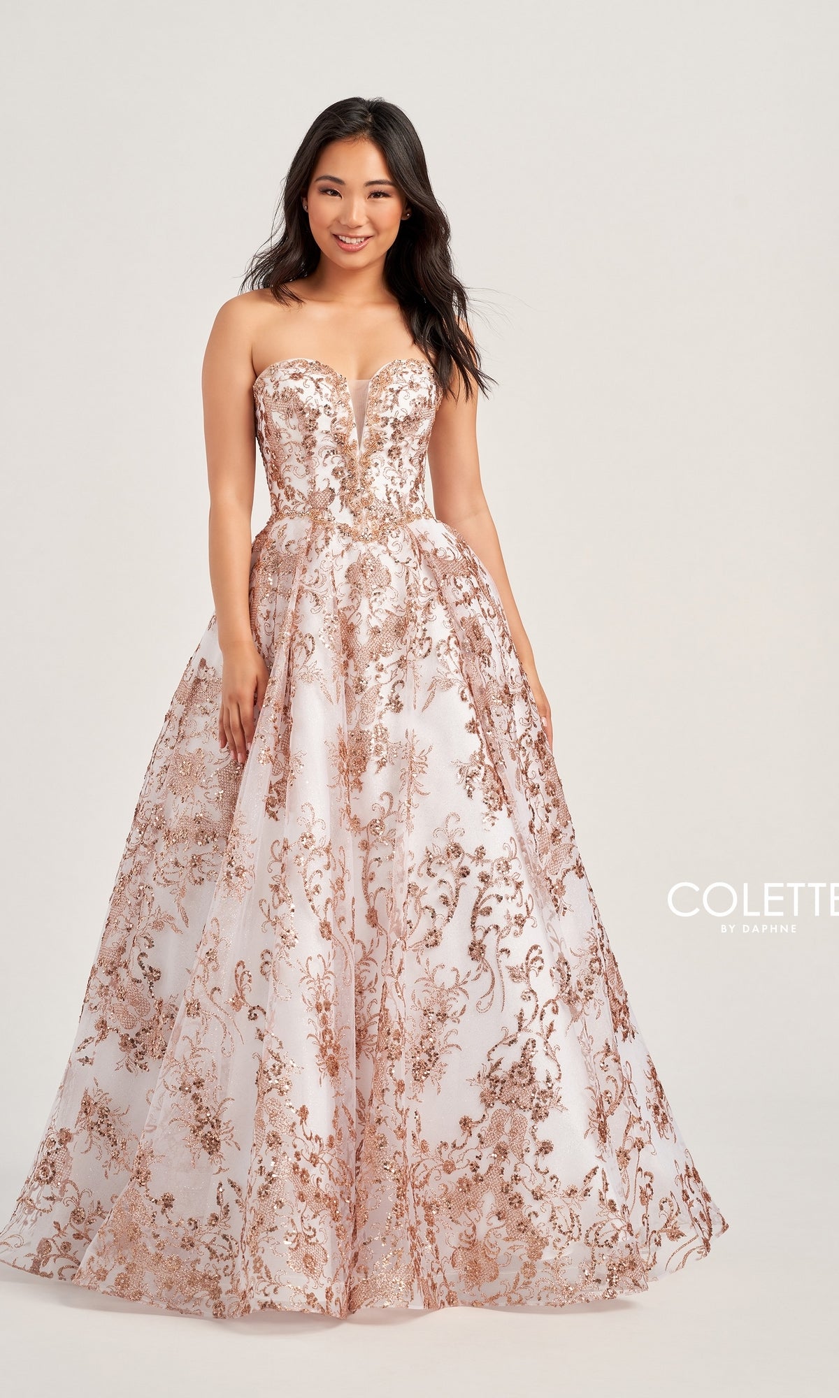 A woman stands and smiles against a plain background in the Colette Strapless Long Prom Ball Gown CL5101, featuring a white base with rose gold floral embroidery that showcases timeless elegance.